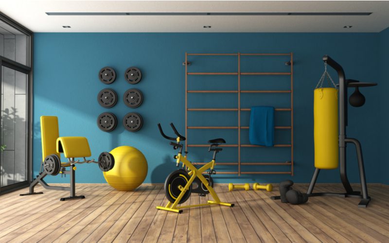 Идея холостяцкой площадки с желтым велотренажером, желтой боксерской грушей и желтой скамьей в окрашенной бирюзовой комнате