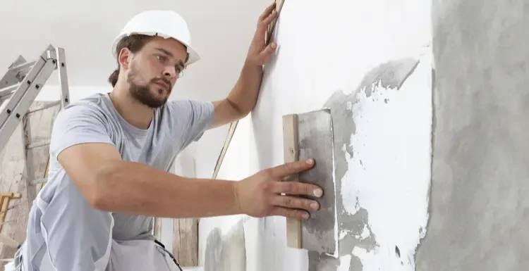 Изображение мужчины, использующего большой шпатель для создания популярного типа текстуры на цементной стене.